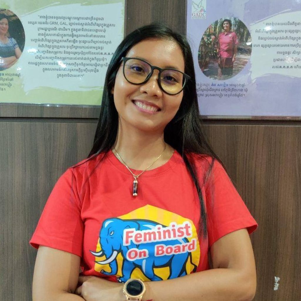 A young woman smiles and stands with her arms folded