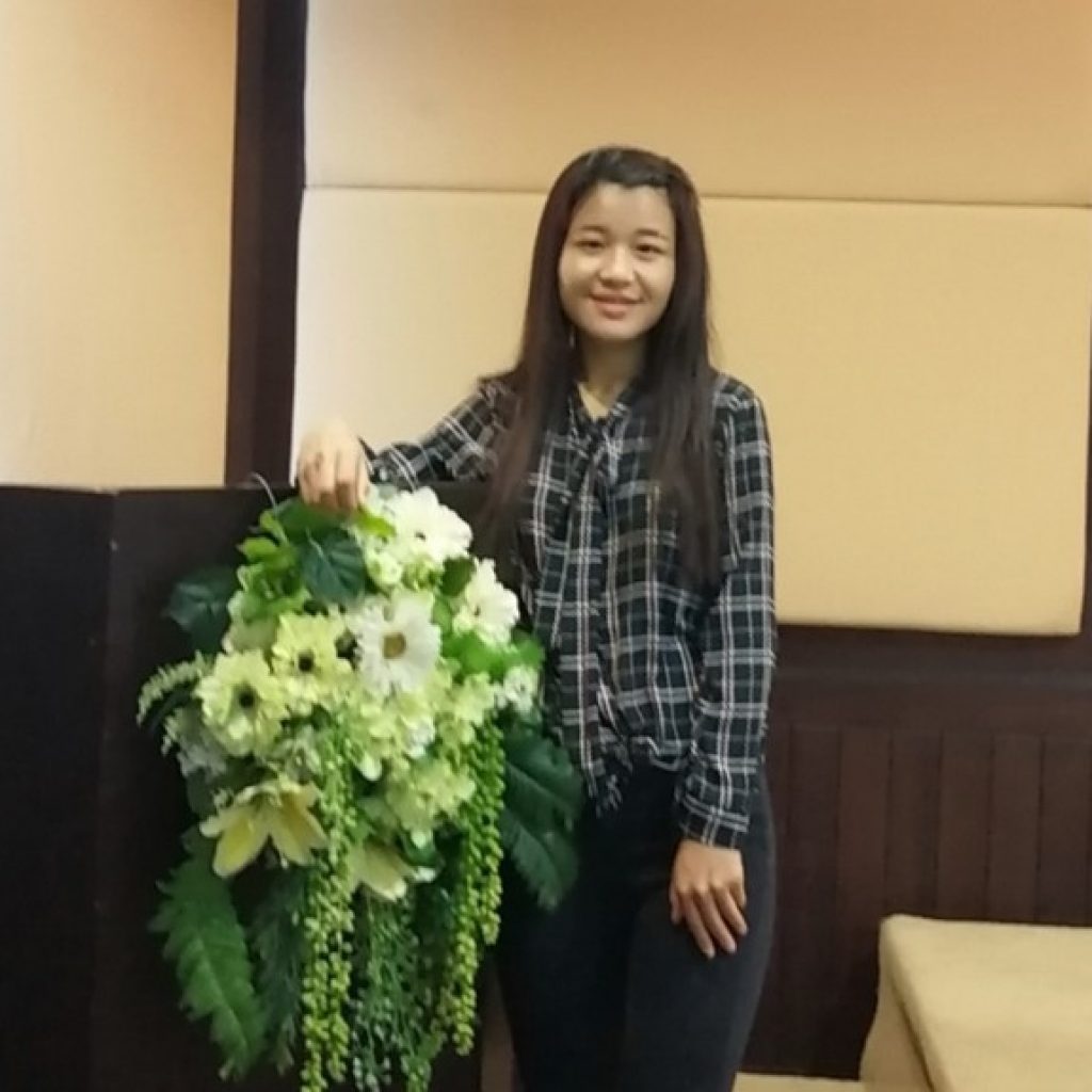 A young woman stands with a wreath of flowers