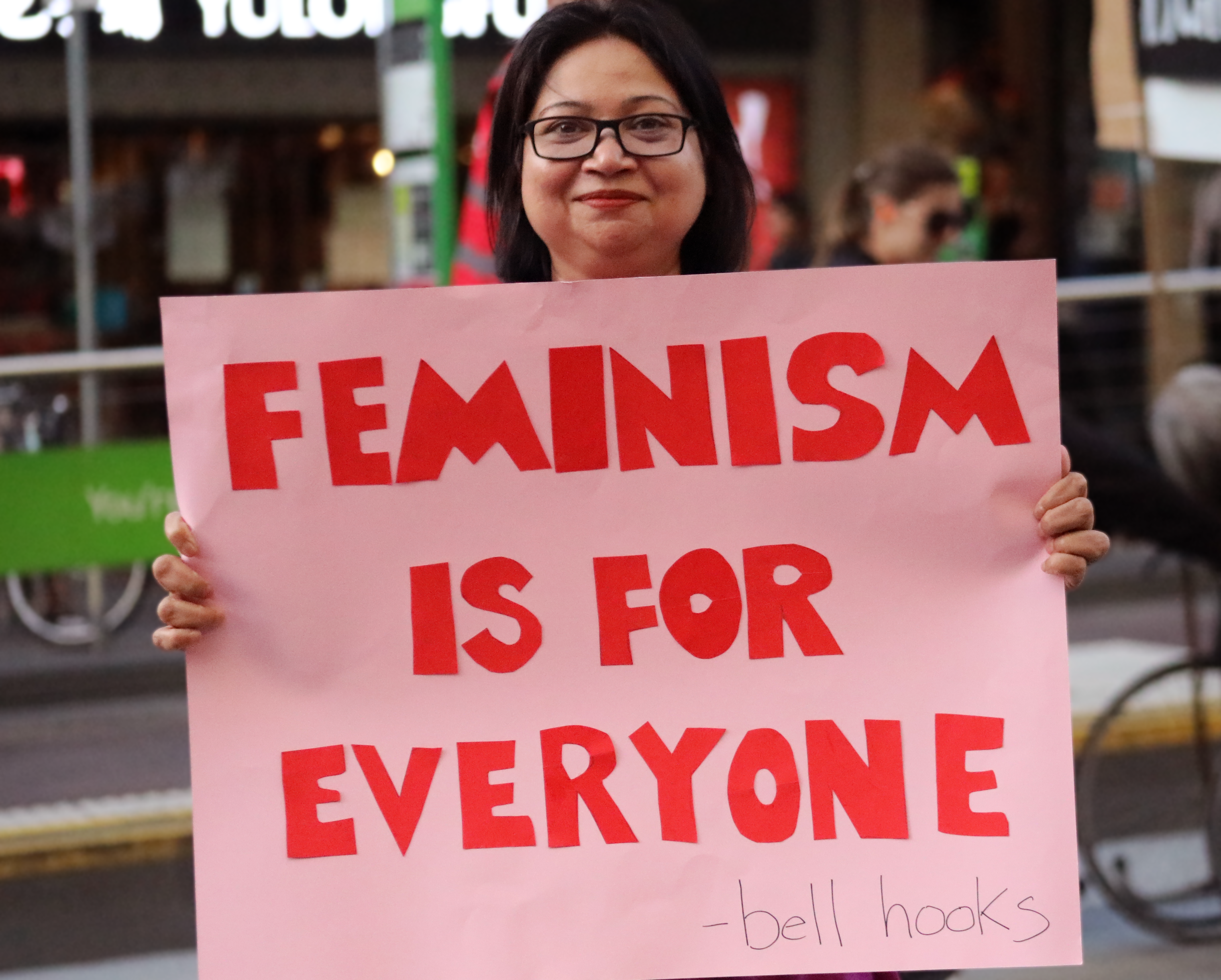 IWDA CEO Nayomi Kannangara at protest holding a pink sign with red lettering. It reads Feminism is for everyone - Bell Hooks.