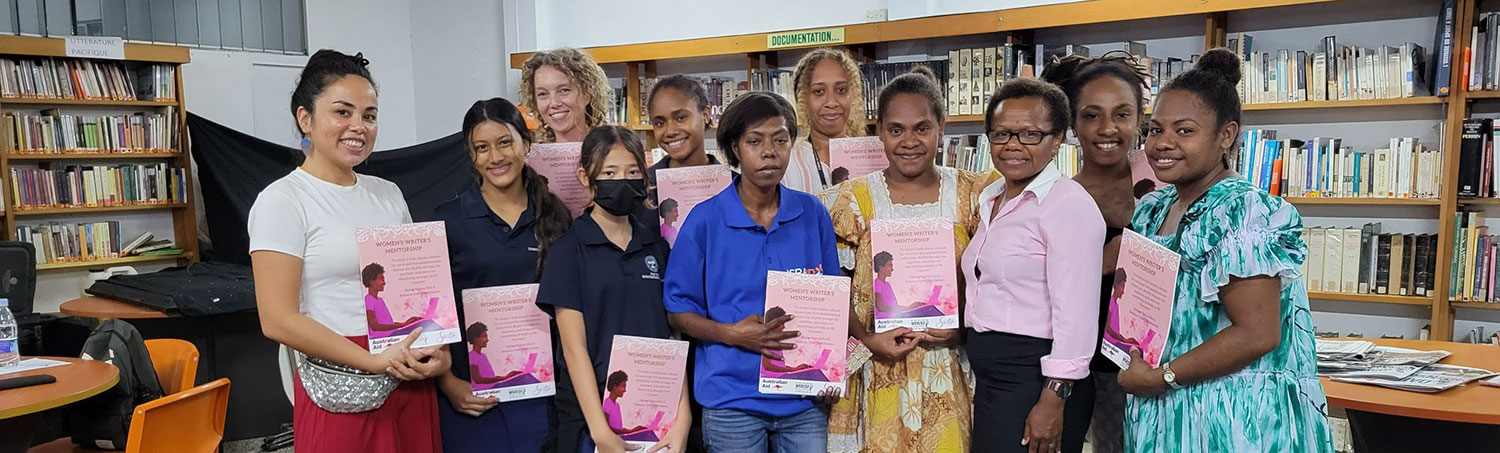 Sista-Womens-Writers-Workshop A group of women stand in a library space holding certificates from a Women Writer's Workshop