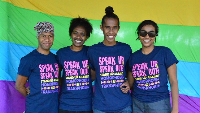 International Day Against Homophobia and Transphobia FWRM supporters stand in front of a rainbow flag.